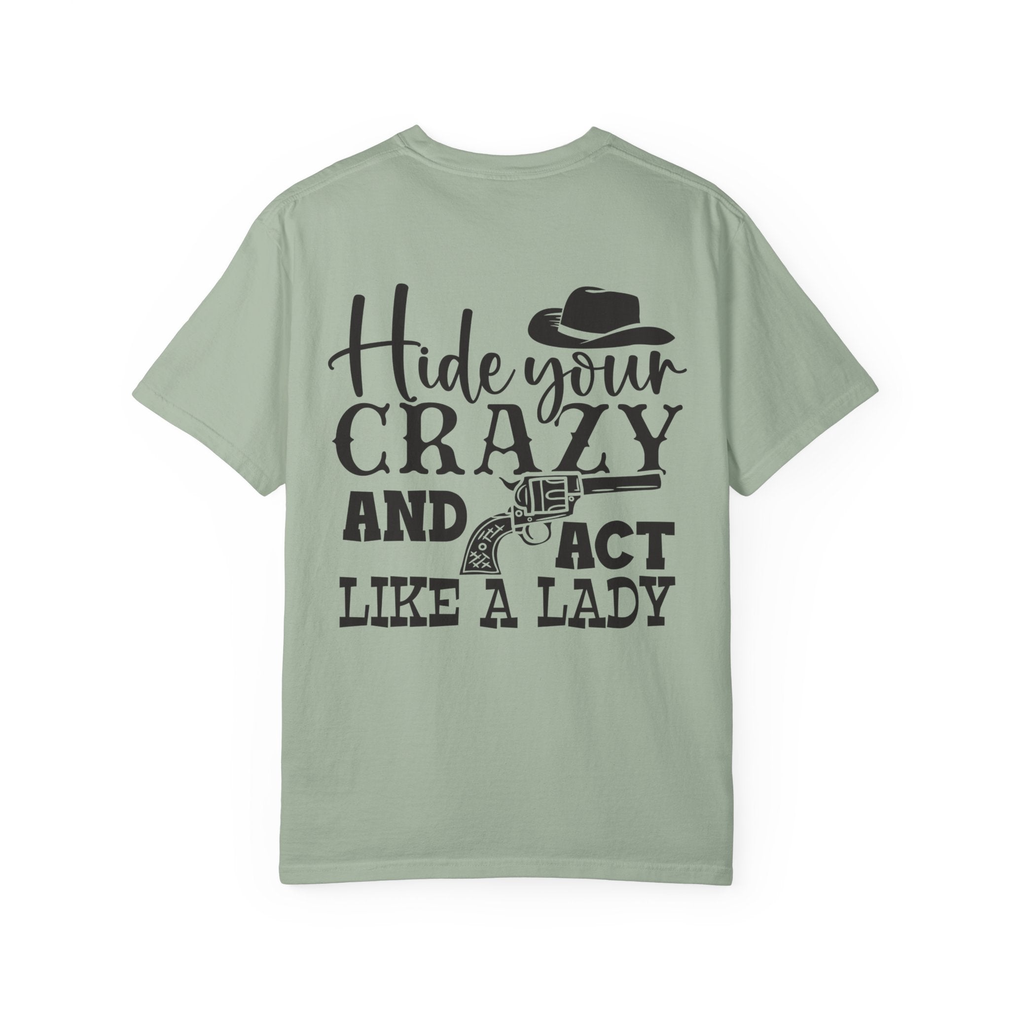 A sage green short-sleeve t-shirt with a black graphic print on the back featuring the text 'Hide your CRAZY AND ACT LIKE A LADY' along with illustrations of a cowboy hat and a revolver, shown against a plain white background.