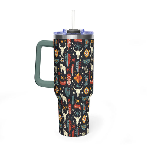 A tall insulated tumbler with a handle and straw, featuring a dark navy background covered in a colorful western-style pattern of skulls, feathers, flowers, and geometric motifs. The handle is muted green, and the lid is clear with a black straw insert.